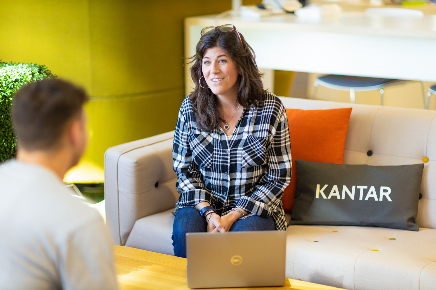 A woman behind a laptop talking to a male colleague